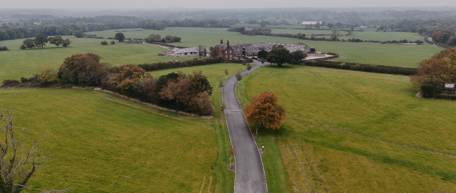 Aerial drone view of green countryside fields and winding road on an overcast day.