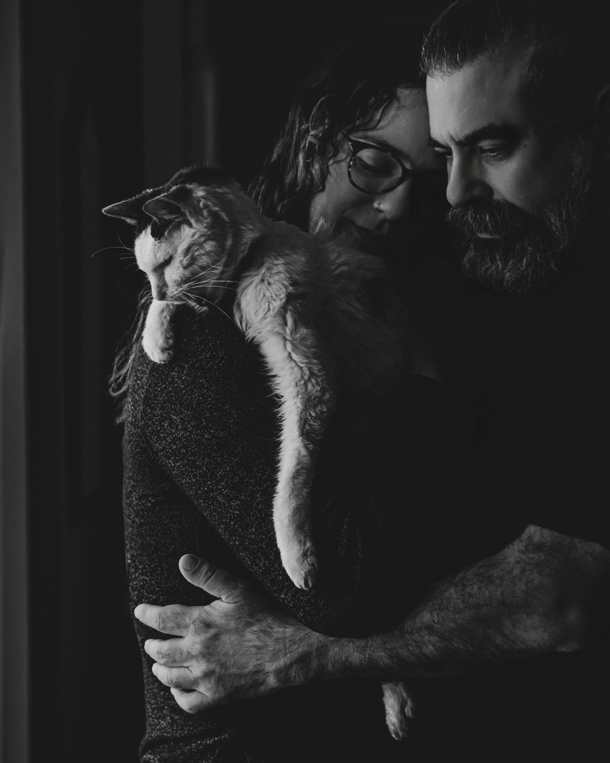 Black and white photo of a couple embracing tenderly while holding a cat between them.