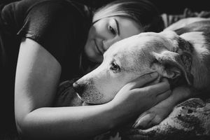 Black and white photo of a young woman tenderly cuddling with a Labrador dog, sharing a peaceful moment.