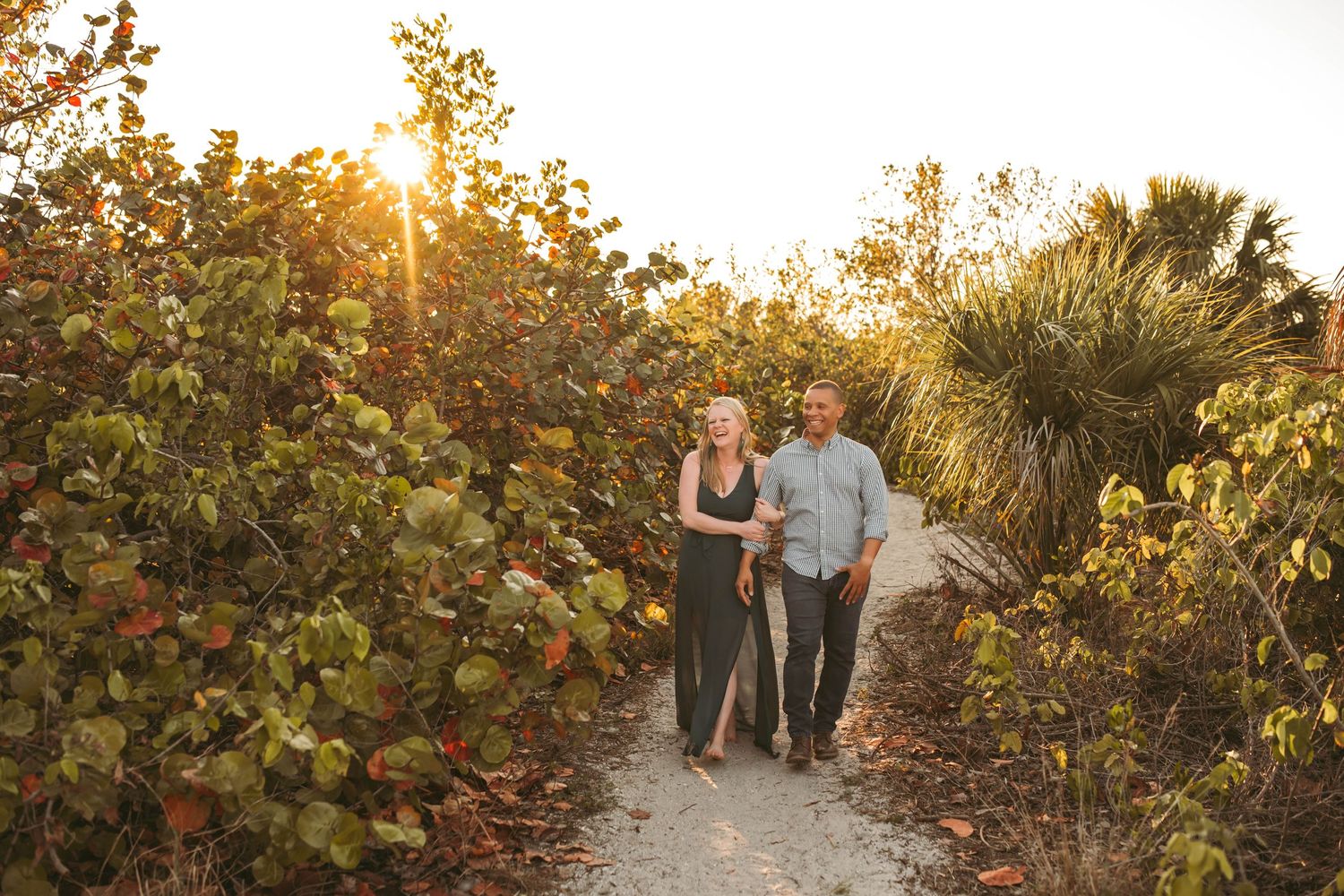 A couple walks along a nature path at sunset with golden light filtering through the trees.