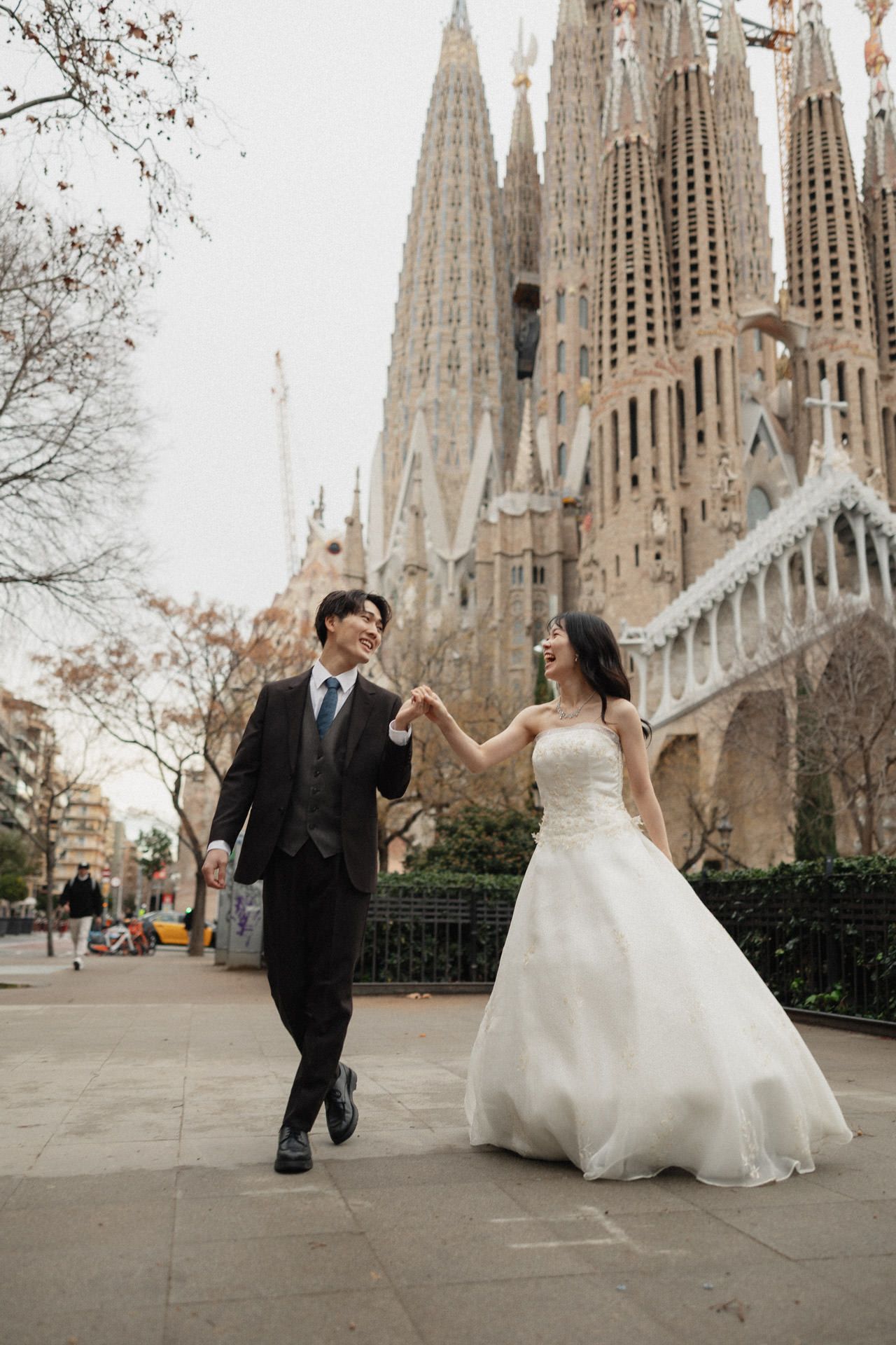 A couple in wedding attire dances and twirls in front of the iconic Sagrada Familia cathedral in Barcelona, Spain.