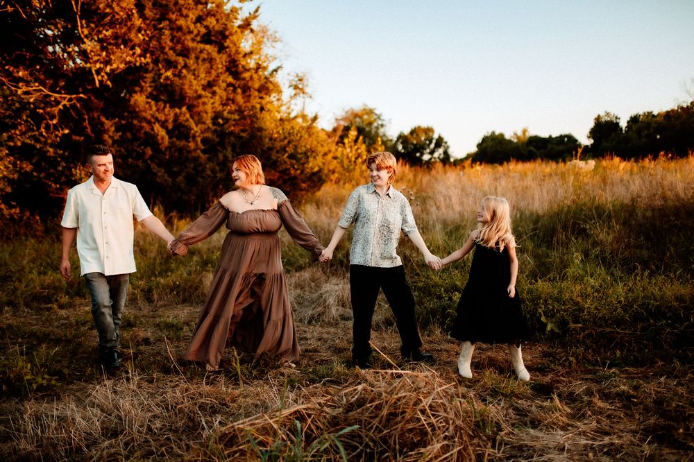 A group of people holding hands while walking through a golden sunlit field at sunset.