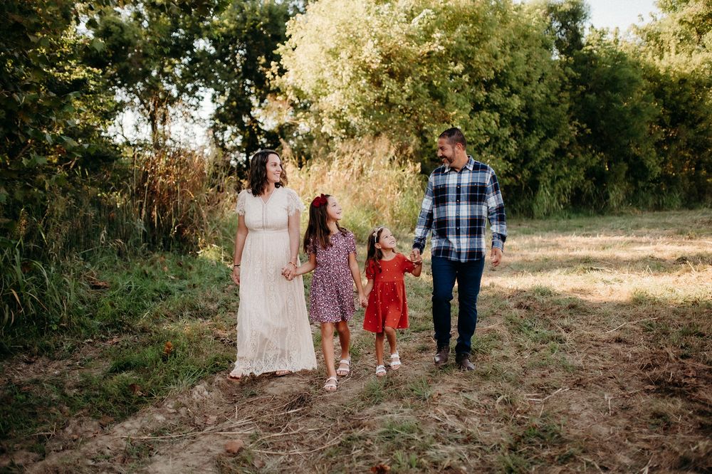 A family of four walks together on a dirt path surrounded by trees and natural scenery during golden hour.