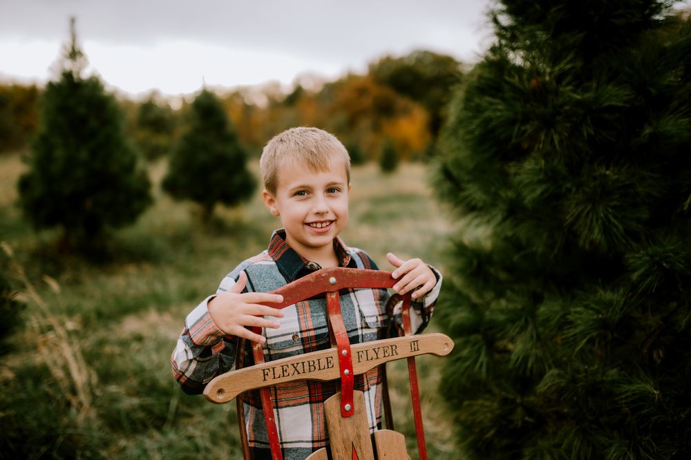 A person wearing a plaid shirt stands in a grassy field during golden hour with autumn trees in the background.