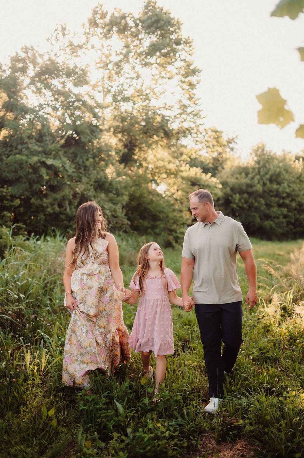 Three people walking together on a nature path at sunset through tall grass and wildflowers in summer.
