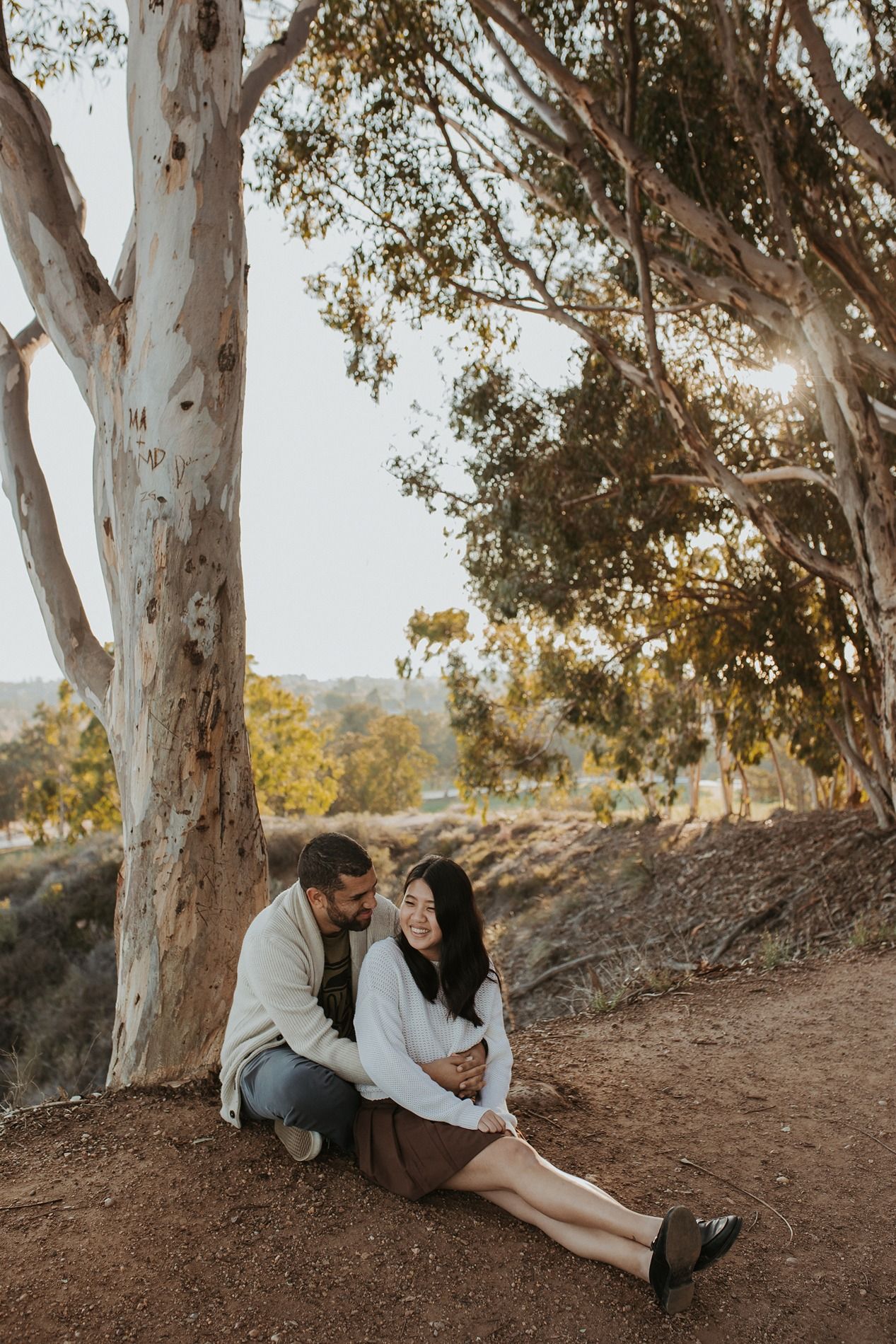 Couple sitting together under tall eucalyptus trees at sunset in a natural outdoor setting at Will Rogers State Park.