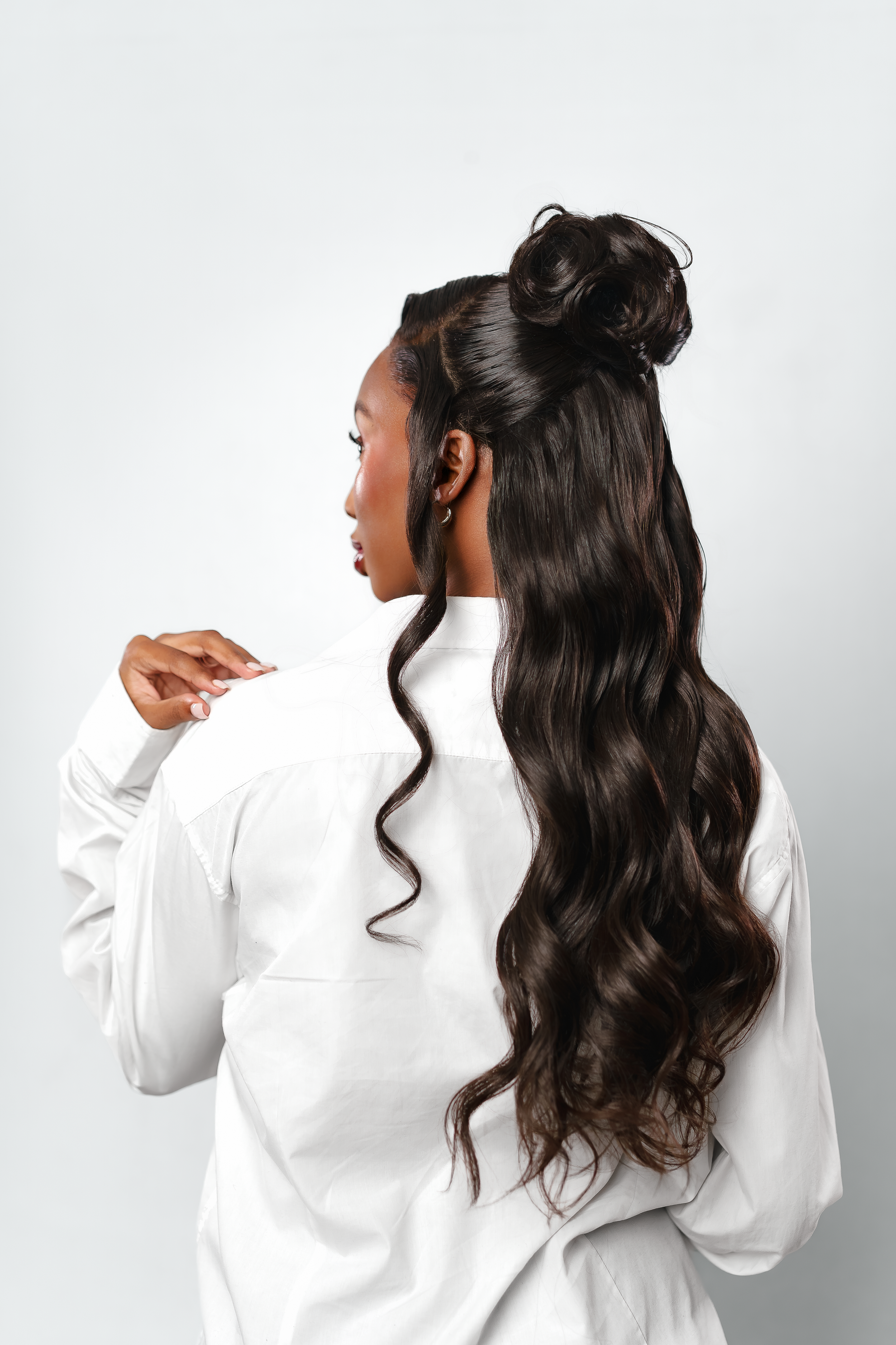 Black woman with long wavy dark hair in half-up bun style, wearing white top, studio photo.