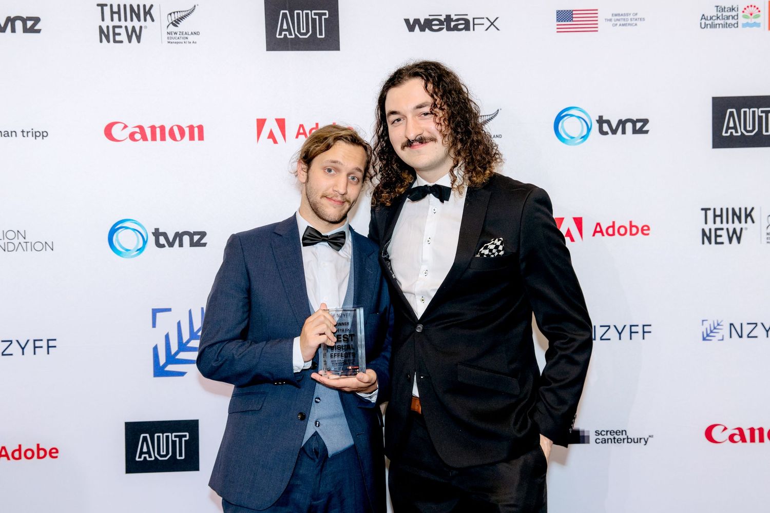 Two award winners posing for the camera in front of a media wall at a corporate event