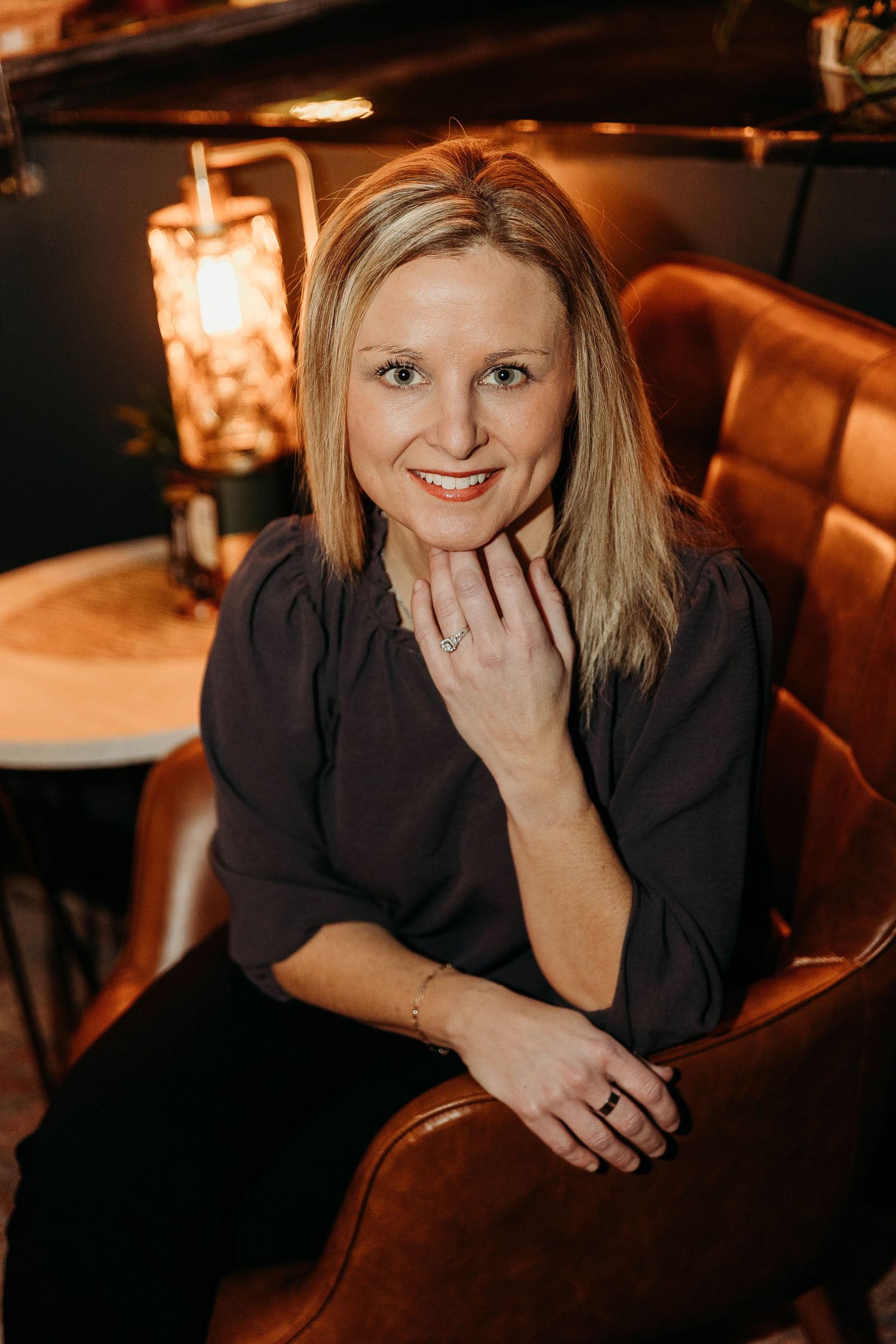 Professional headshots in warm lighting show someone in a black top posing against a dark restaurant backdrop.