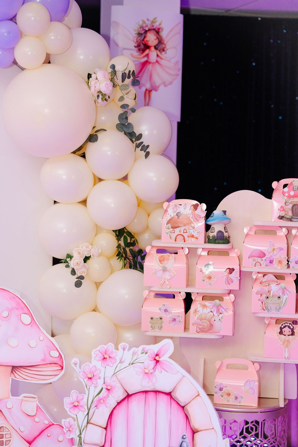 A fairy-themed birthday party display with pink gift boxes, balloon garland, and whimsical mushroom decorations.