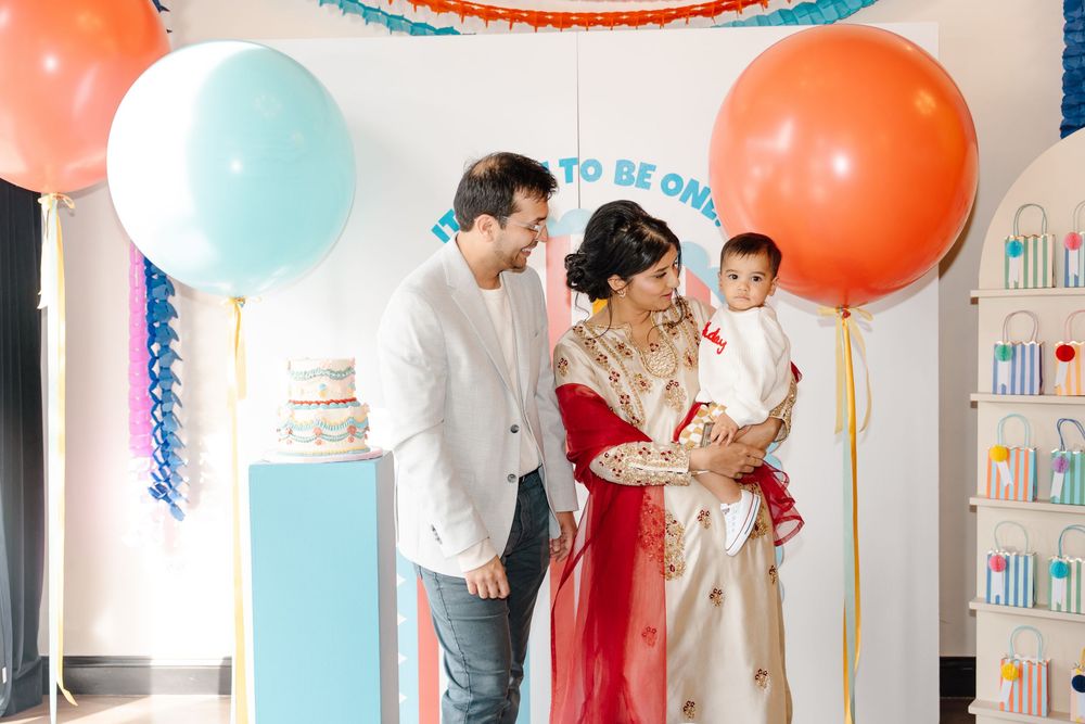 Family celebrates baby's first birthday party with colorful balloons and festive decorations.