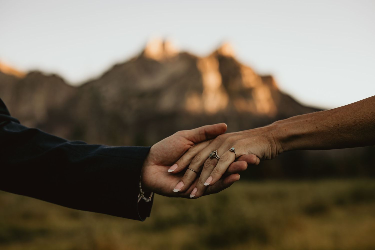 Close-up of hands reaching for each other against a mountain sunset backdrop.