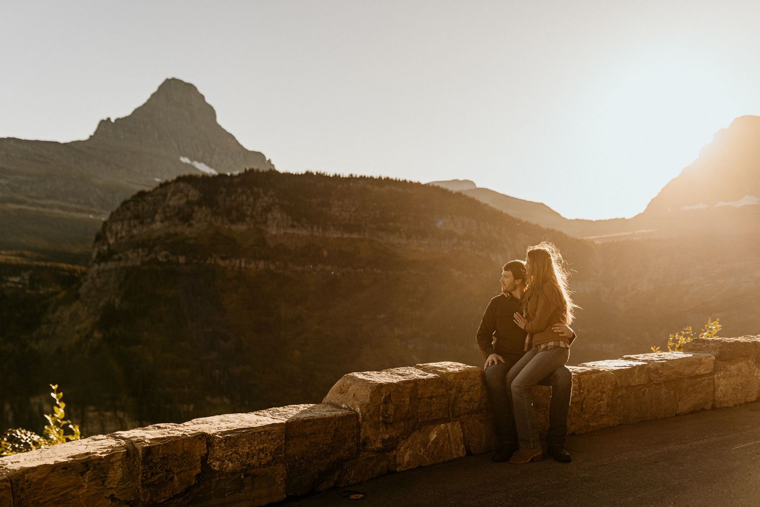 Two silhouettes stand together against a dramatic mountain landscape during golden hour.