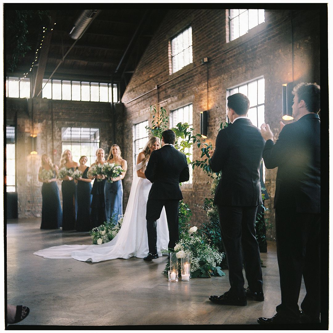 A wedding ceremony in a rustic industrial venue with exposed brick walls and natural light streaming through windows.