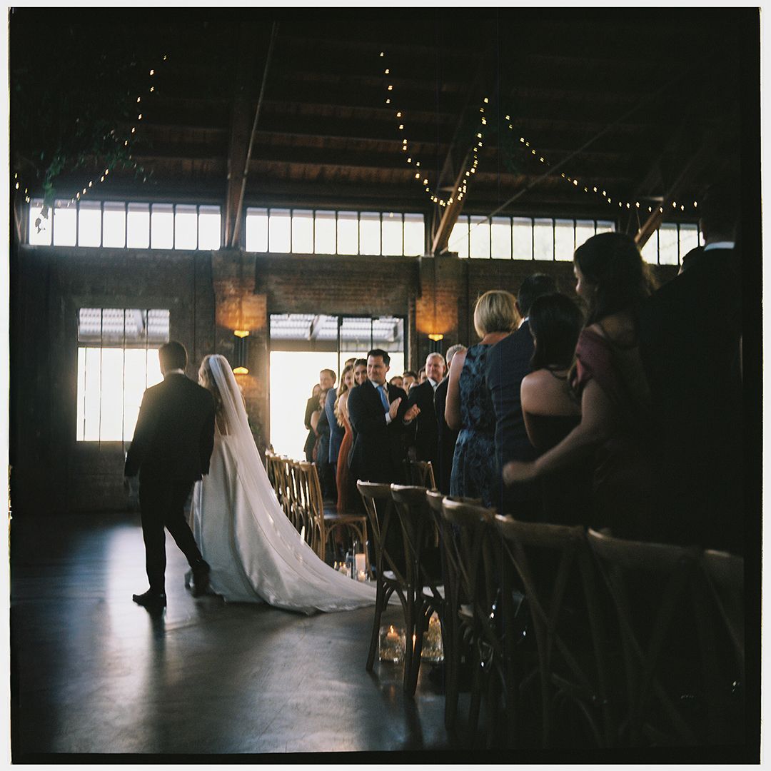 A wedding ceremony takes place in a dimly lit rustic venue with guests seated in wooden chairs.