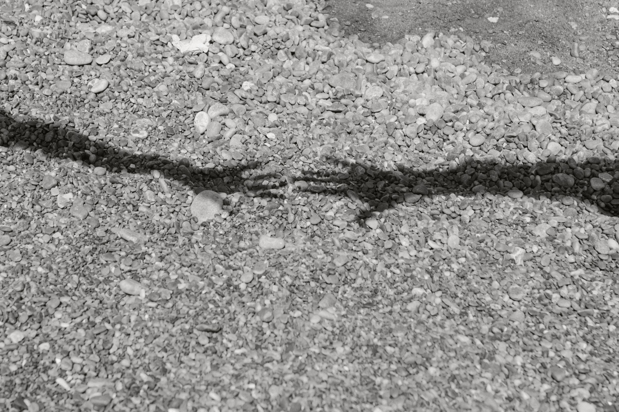 Close-up view of rough textured asphalt or concrete surface showing cracks and weathered patterns.