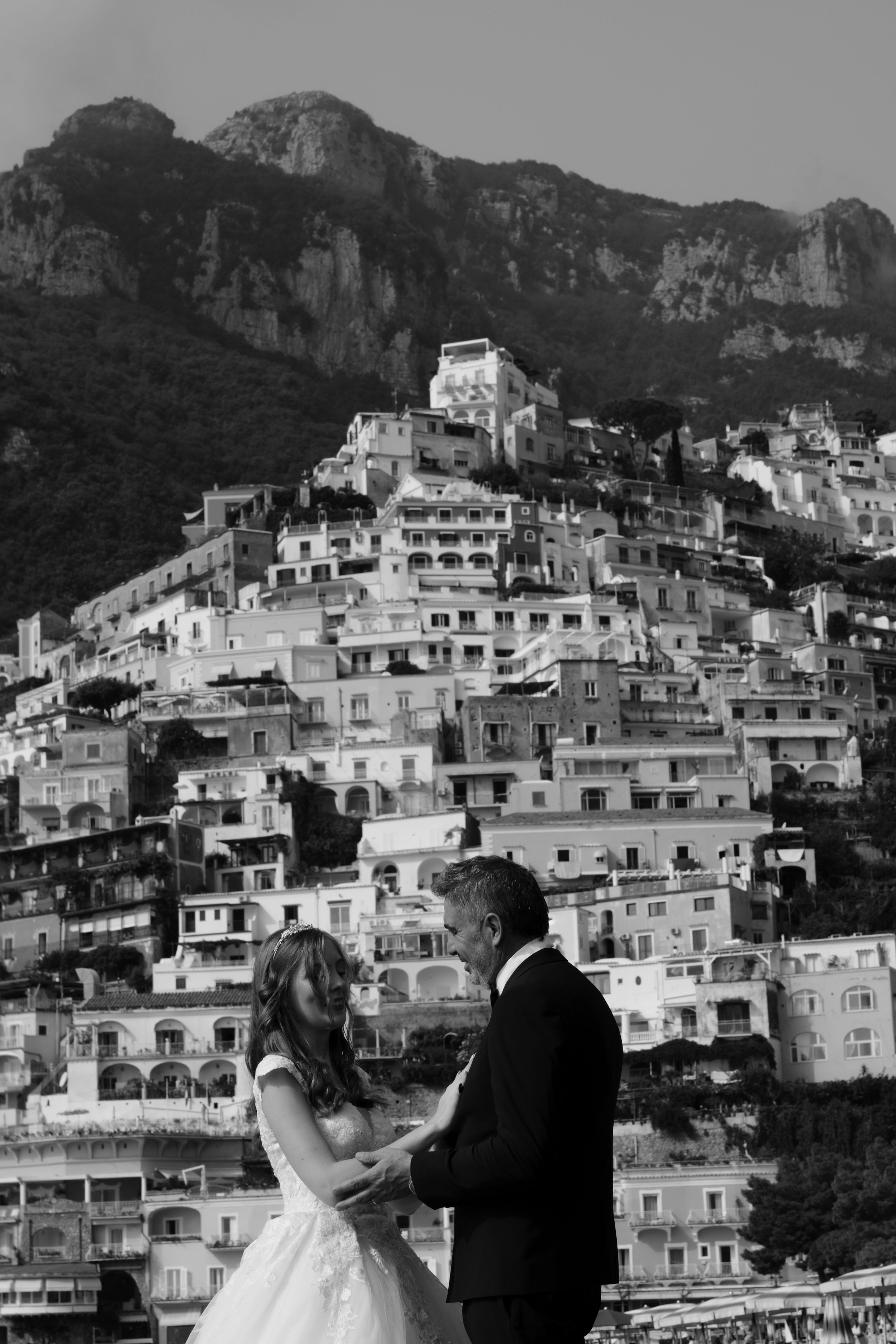 A couple stands against the scenic backdrop of white hillside buildings in Positano, Italy during their wedding day.