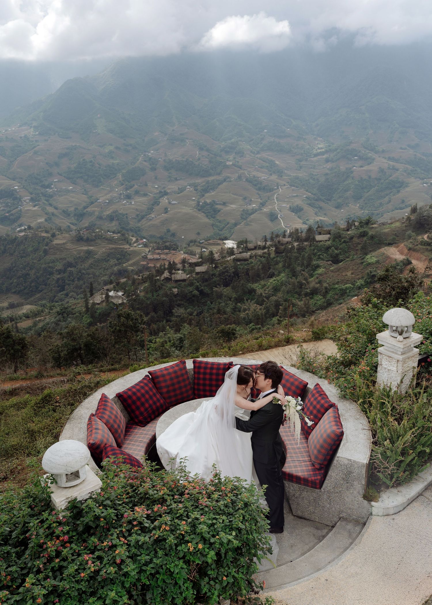 Bride and groom sharing a romantic moment on a circular terrace overlooking stunning mountain valleys.