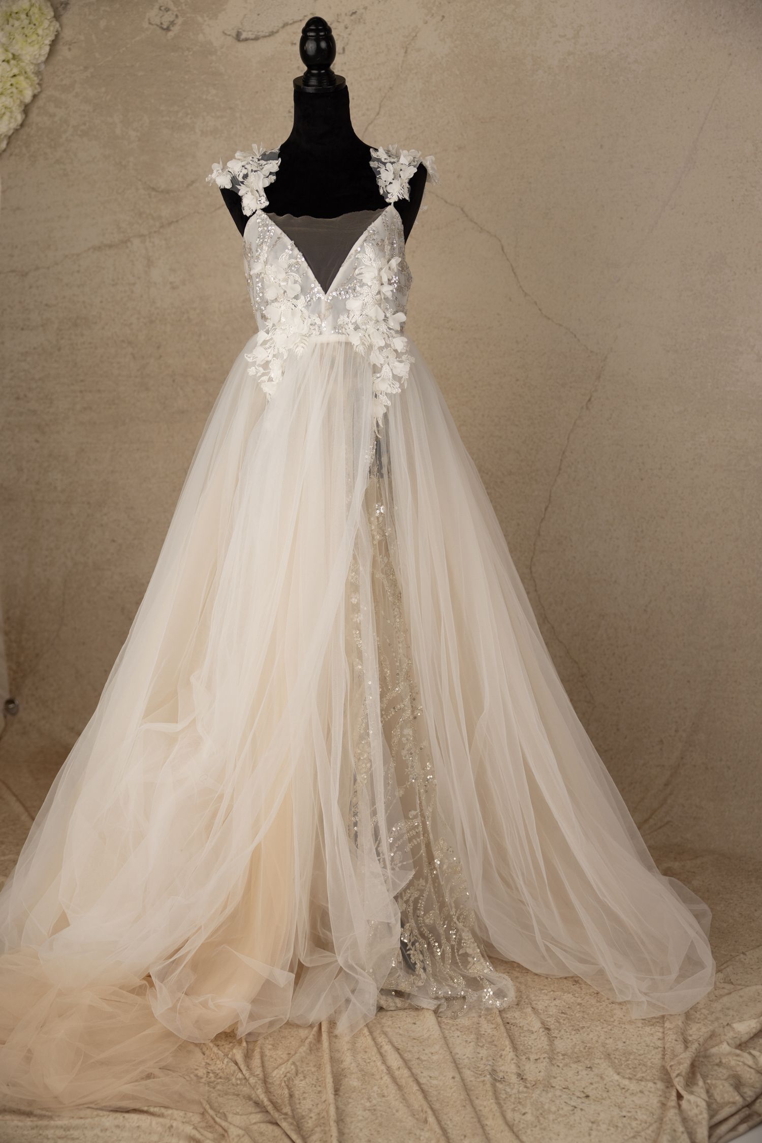 Ethereal ivory wedding dress with floral appliques and flowing tulle skirt displayed against neutral backdrop.