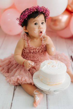 Baby in pink tulle dress having a cake smash photo session with white frosting穿著粉紅色薄紗洋裝的寶寶正在拍攝蛋糕砸臉照，蛋糕上還沾滿了白色糖霜。