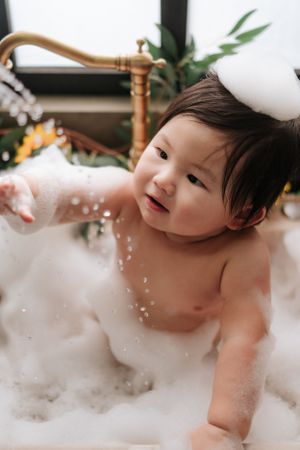 Baby enjoying bath time with bubbles and smiles in a white bathtub.寶寶在白色浴缸裡享受泡泡浴，臉上洋溢著笑容。