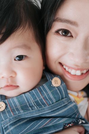 Close up portrait of parent and small child wearing denim overalls smiling at camera together.父母和穿著牛仔背帶褲的小孩一起對著鏡頭微笑，這是一張特寫肖像照。