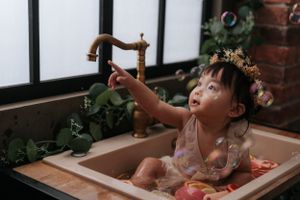 Creative bath time photo shoot with flowers and bubbles in natural window light.在自然窗光下，用鮮花和泡泡拍攝創意沐浴照。