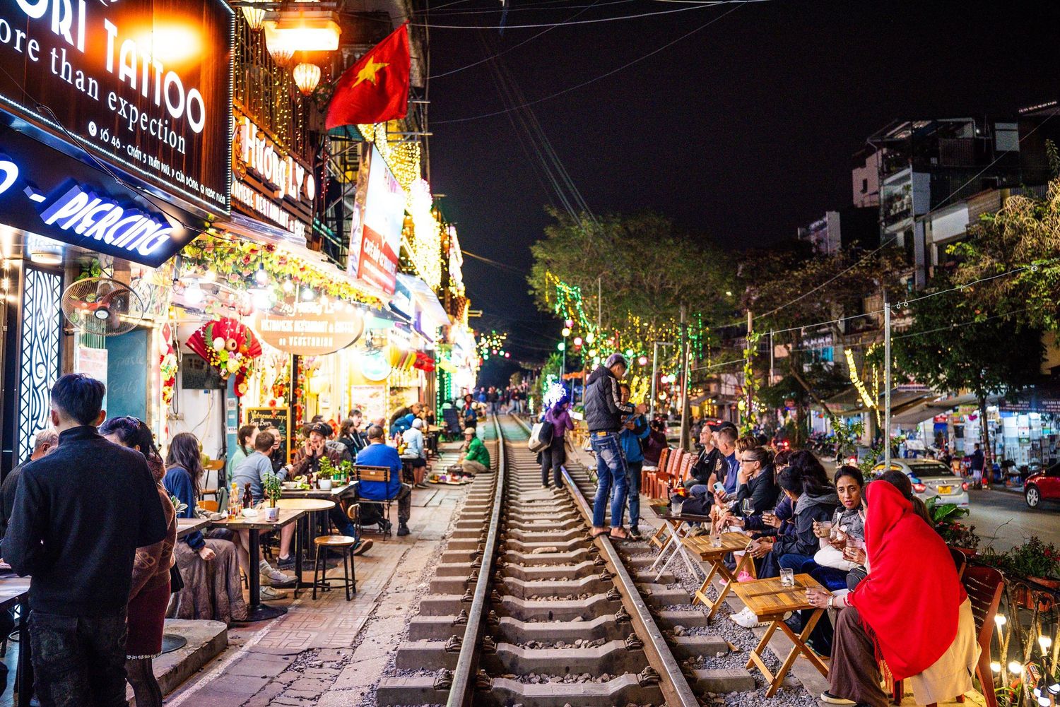 Bustling nightlife scene along railway tracks in Hanoi's Train Street with illuminated restaurants and cafes.