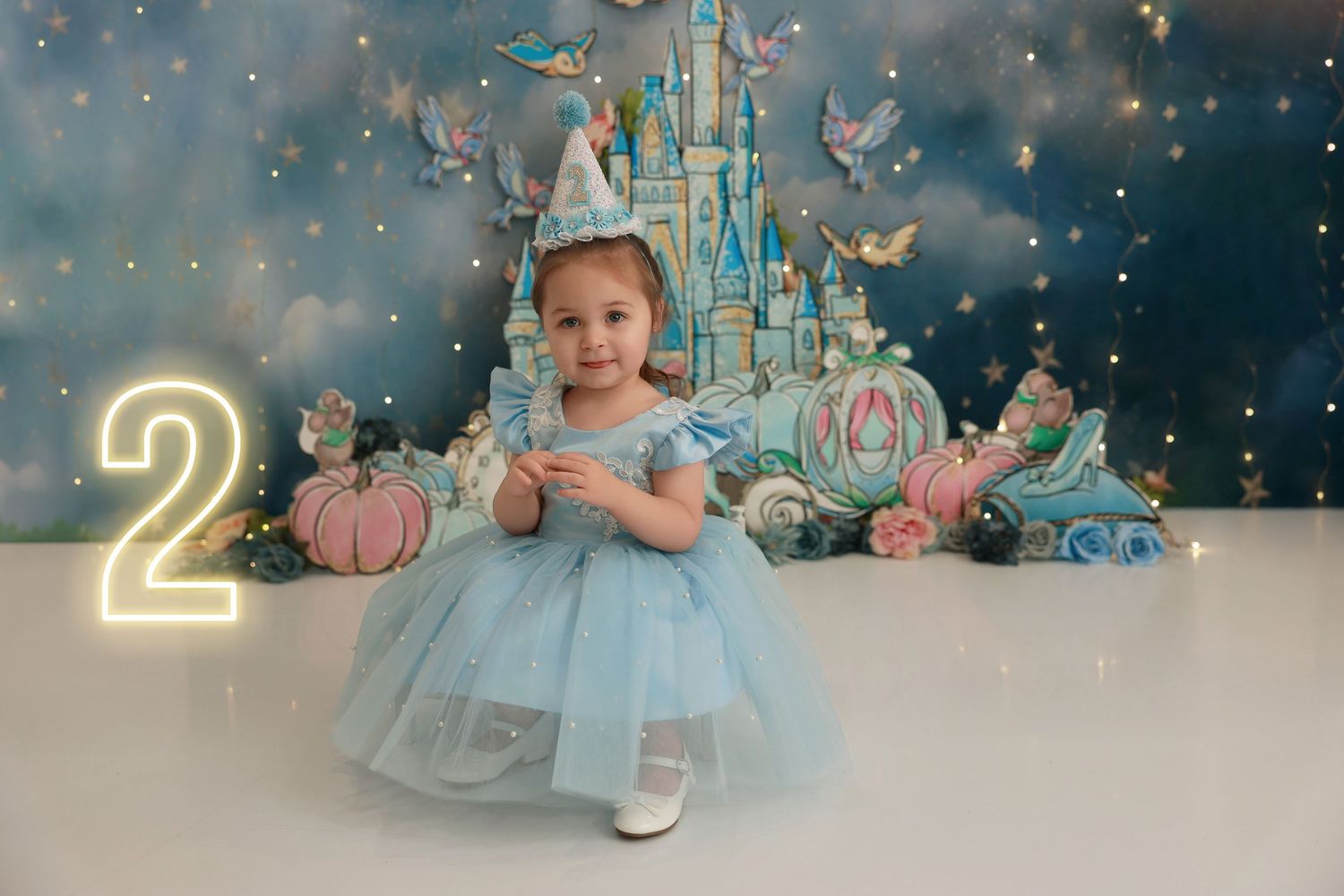 A magical Cinderella themed photo session with twinkling lights, pumpkins, and blue tulle dress against a dark backdrop.