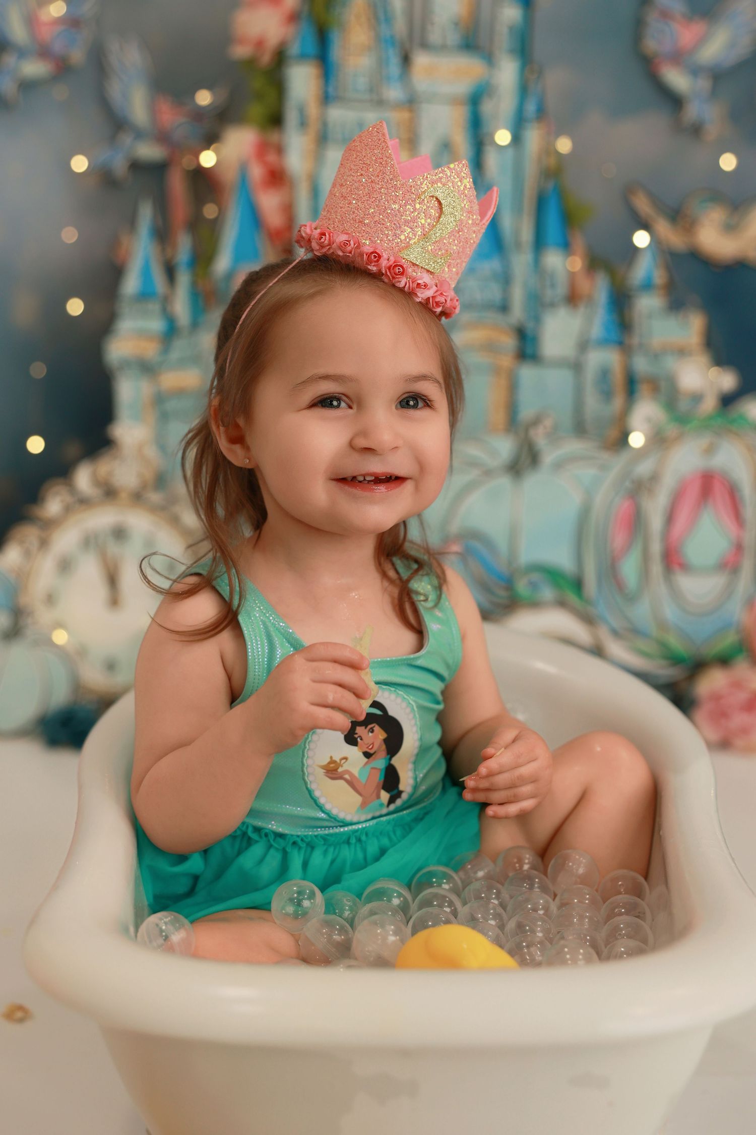 A child in a turquoise dress sits in a bubble bath with twinkling lights and decorative elements in the background.
