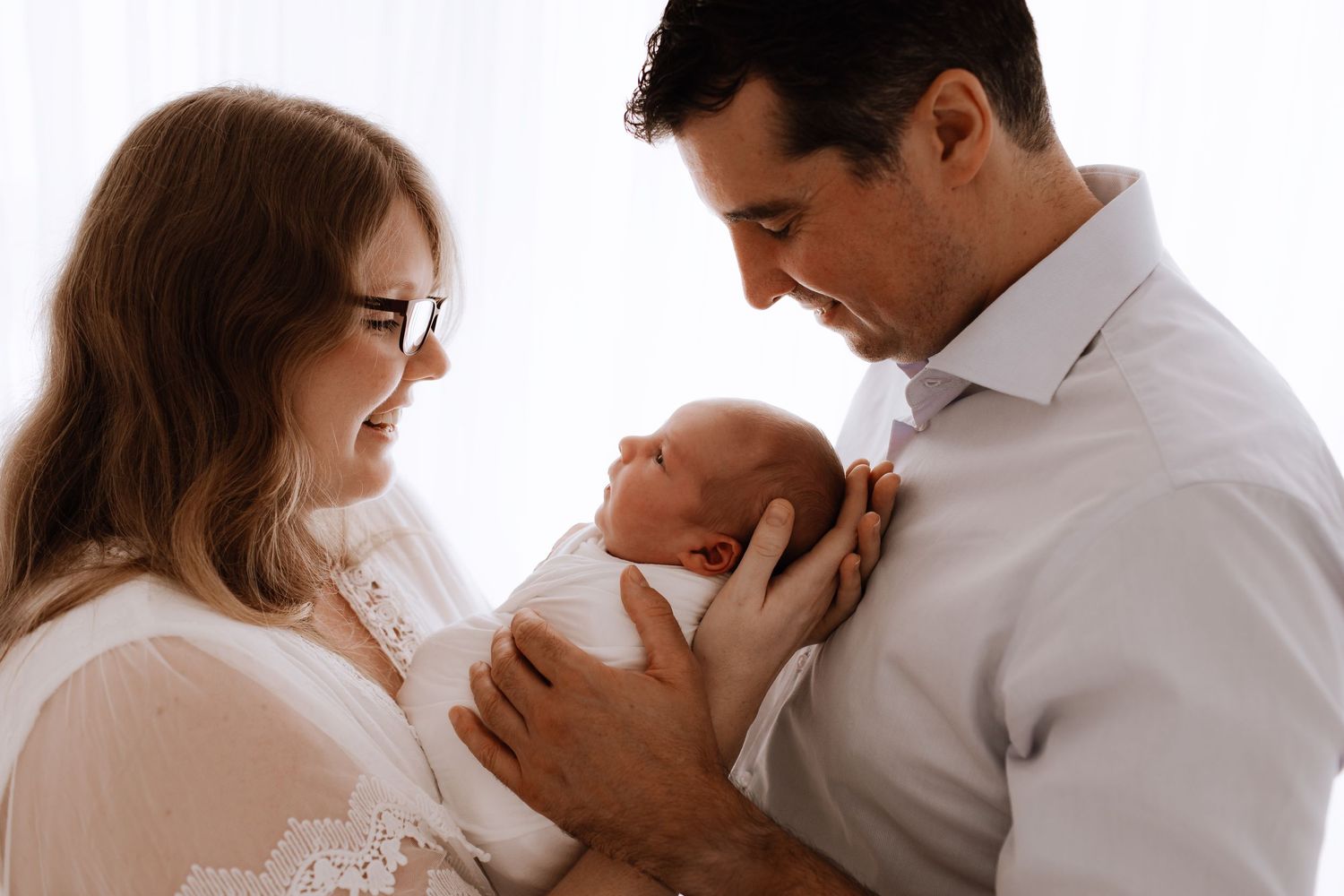Studio family session with white clothing showing tender moments with newborn.
