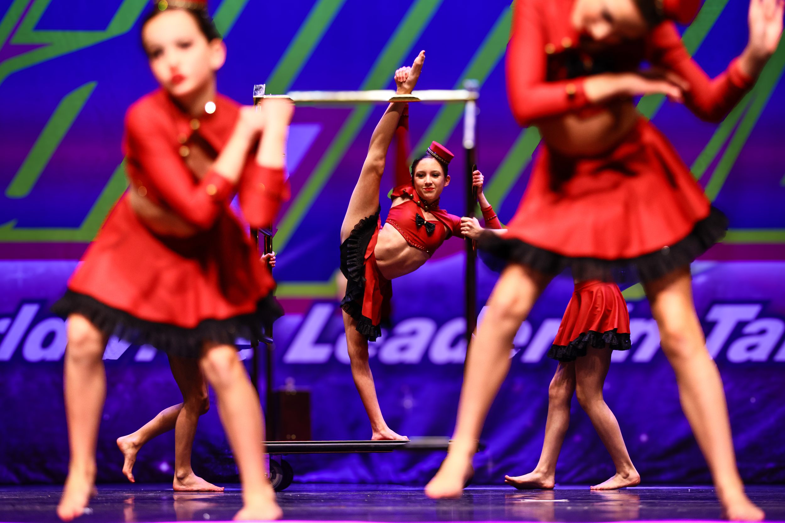 Young female dancer performing an impressive leg extension in red costume on competition stage.