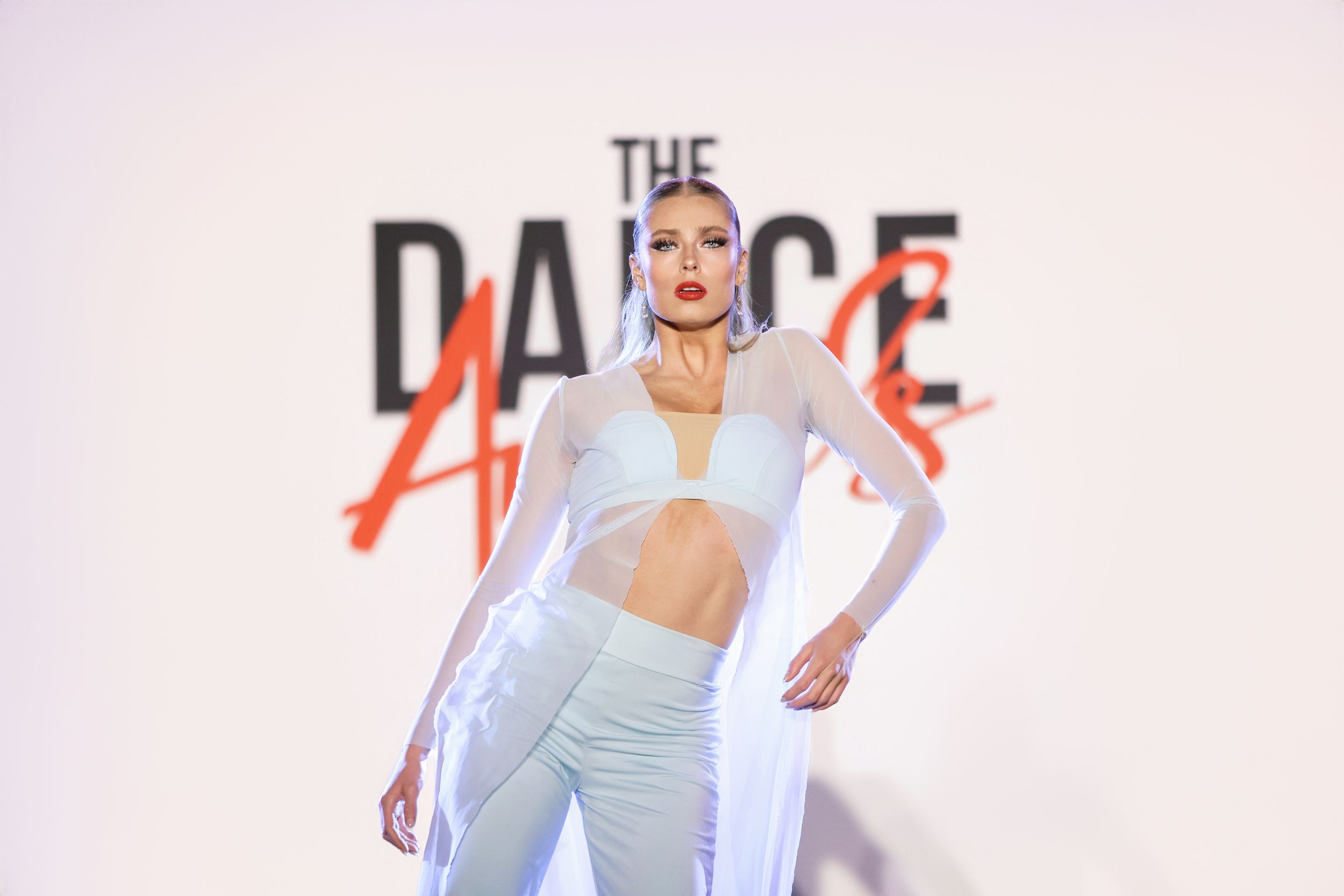 Female dancer in white outfit posing confidently in front of The Dance Awards backdrop.