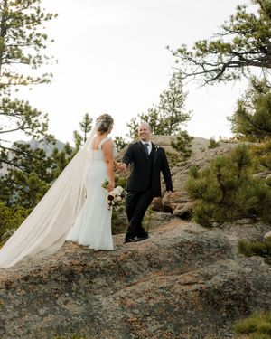 A bride and groom share a romantic moment on a rocky mountain overlook surrounded by pine trees on their wedding day.