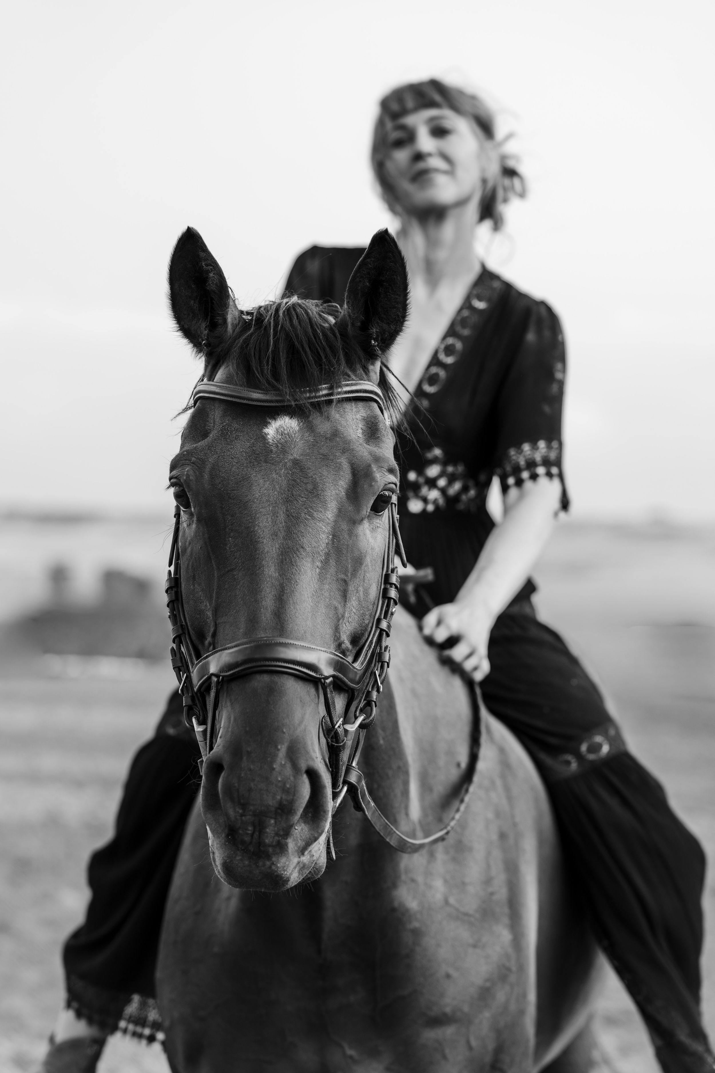 Black and white photo of a woman in dark clothing riding a horse in an open field.