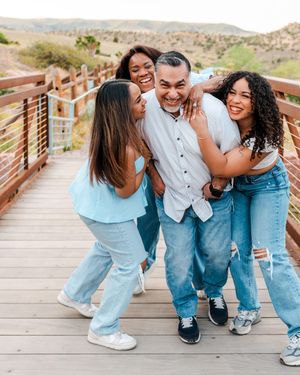 Happy family of four laughing and hugging on a wooden bridge outdoors in casual blue and white outfits.