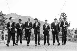 Groomsmen walking together in black suits with mountain backdrop at outdoor wedding venue.