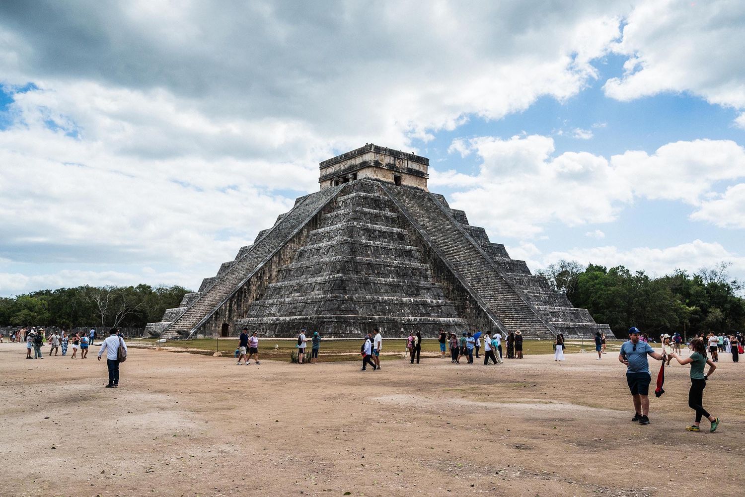 Tourists explore the ancient Mayan pyramid of Chichen Itza under cloudy skies in Mexico.