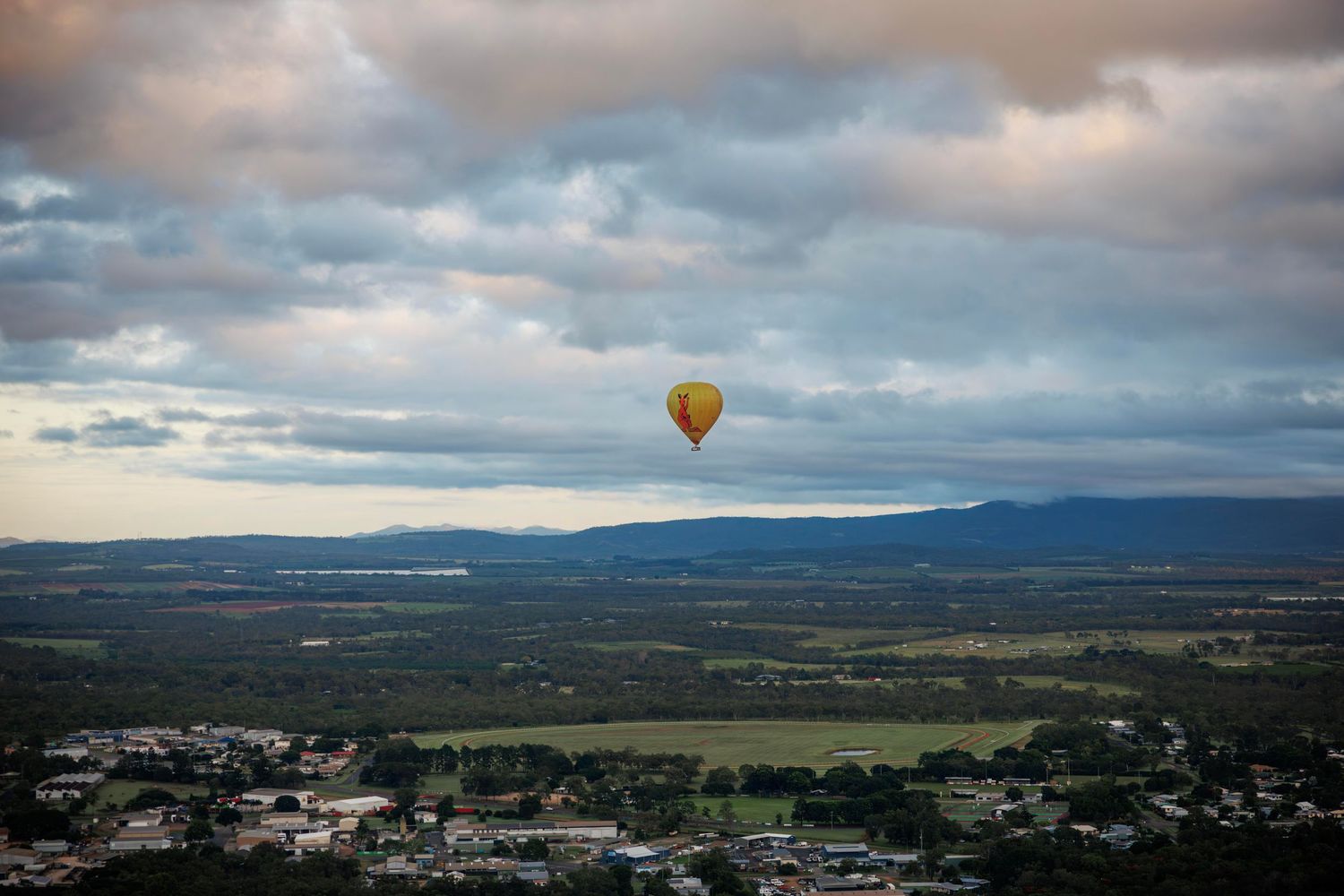 Yellow hot air balloon floating over a vast green valley landscape under dramatic cloudy skies. Cairns Australia
