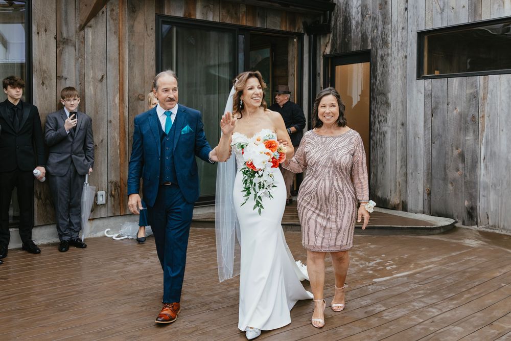 Wedding party members walk and celebrate together outside a rustic wooden barn venue.