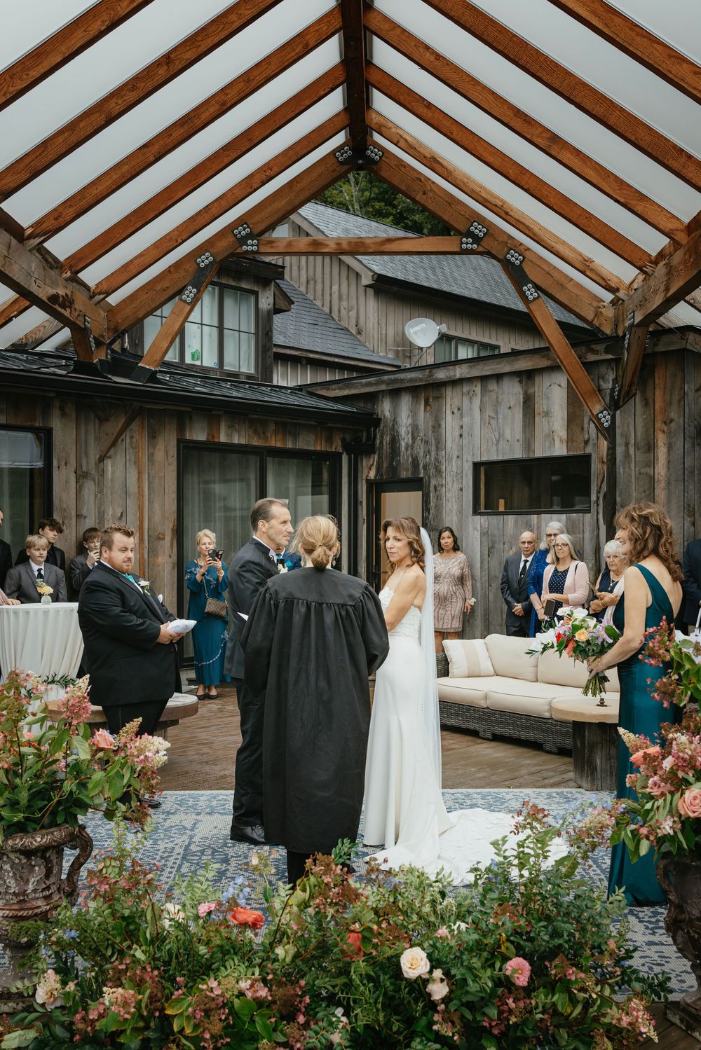 Wedding guests gather in a rustic wooden greenhouse venue with exposed beams and beautiful rose gardens.