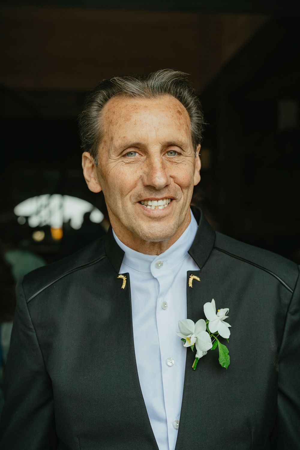 Close-up portrait of someone wearing a black suit jacket and white shirt with a white boutonniere.