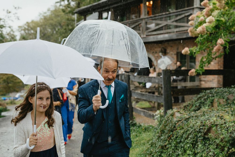 A couple shares an intimate moment under umbrellas in the rain during an outdoor wedding celebration.