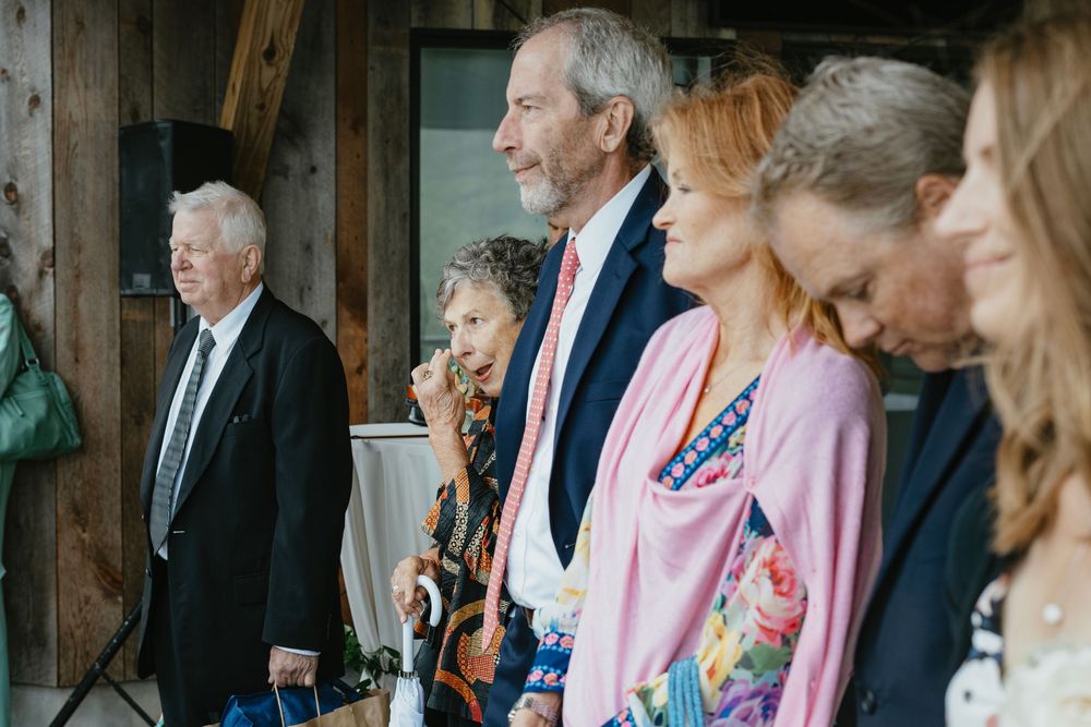 Wedding guests seated in rows at an indoor venue with rustic wooden beams and natural lighting.