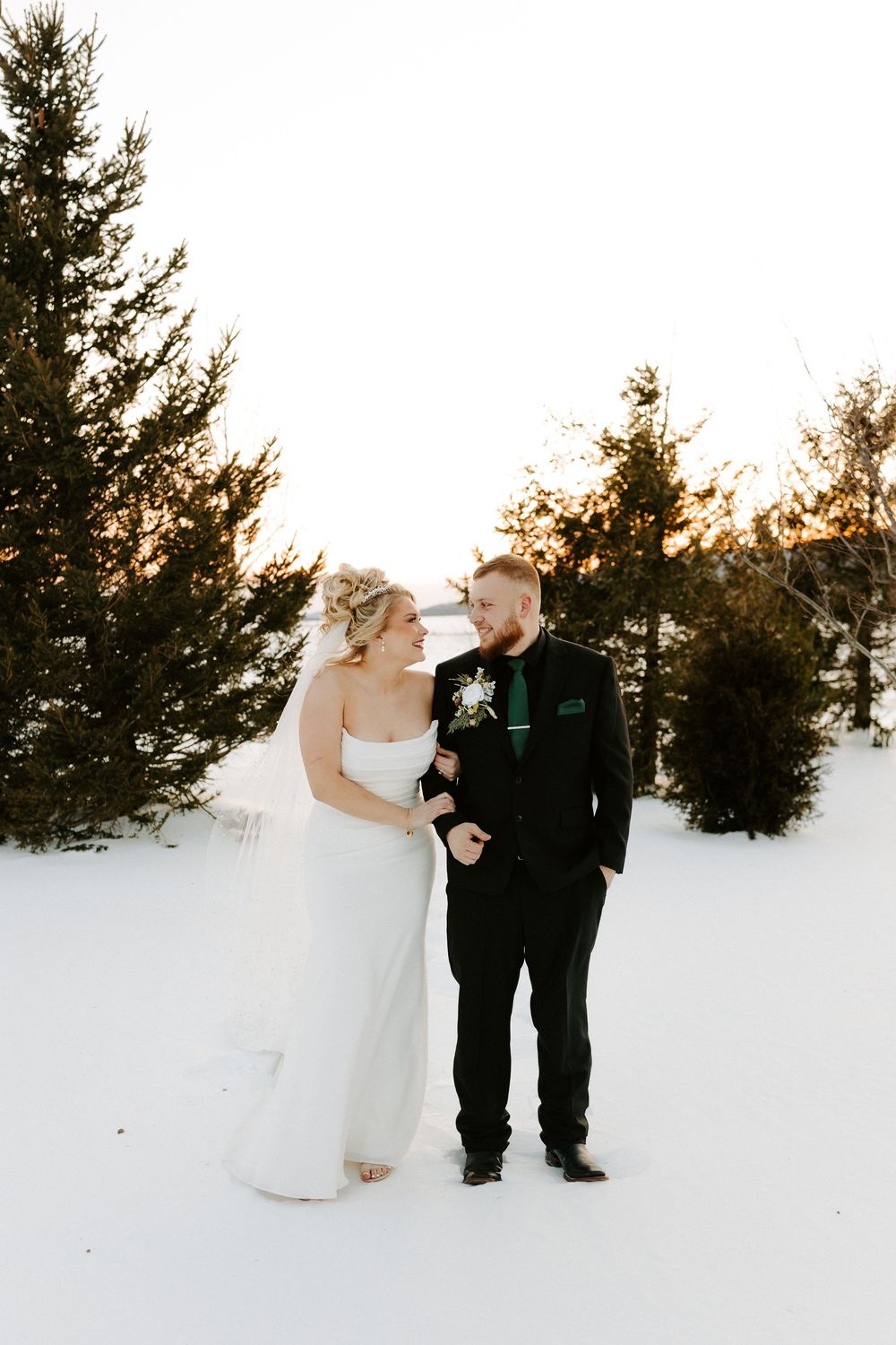 Bride and groom share a joyful moment in a snowy winter landscape surrounded by evergreen trees.