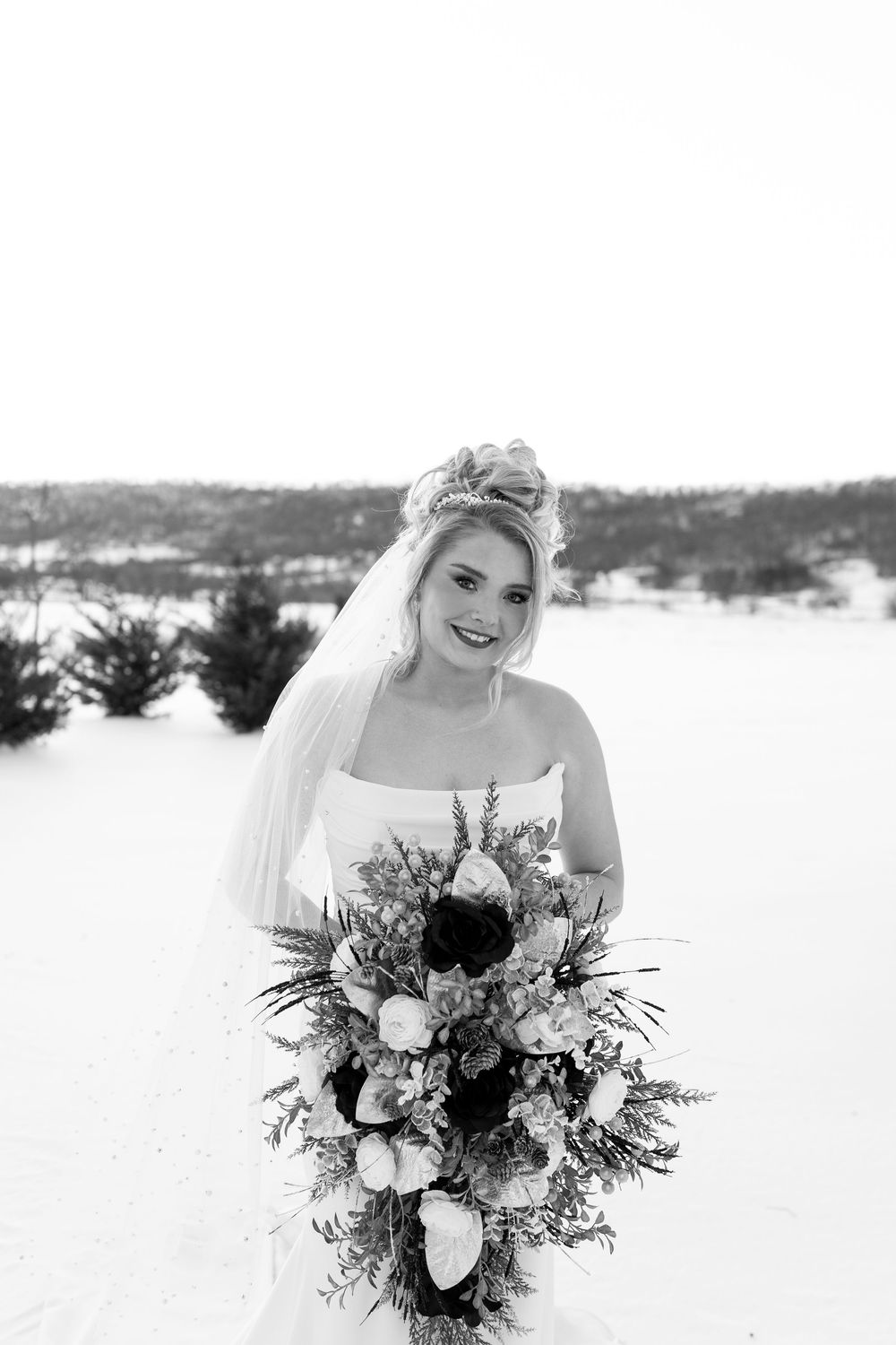 Black and white portrait of a bride holding a cascading winter bouquet in a snowy outdoor setting.