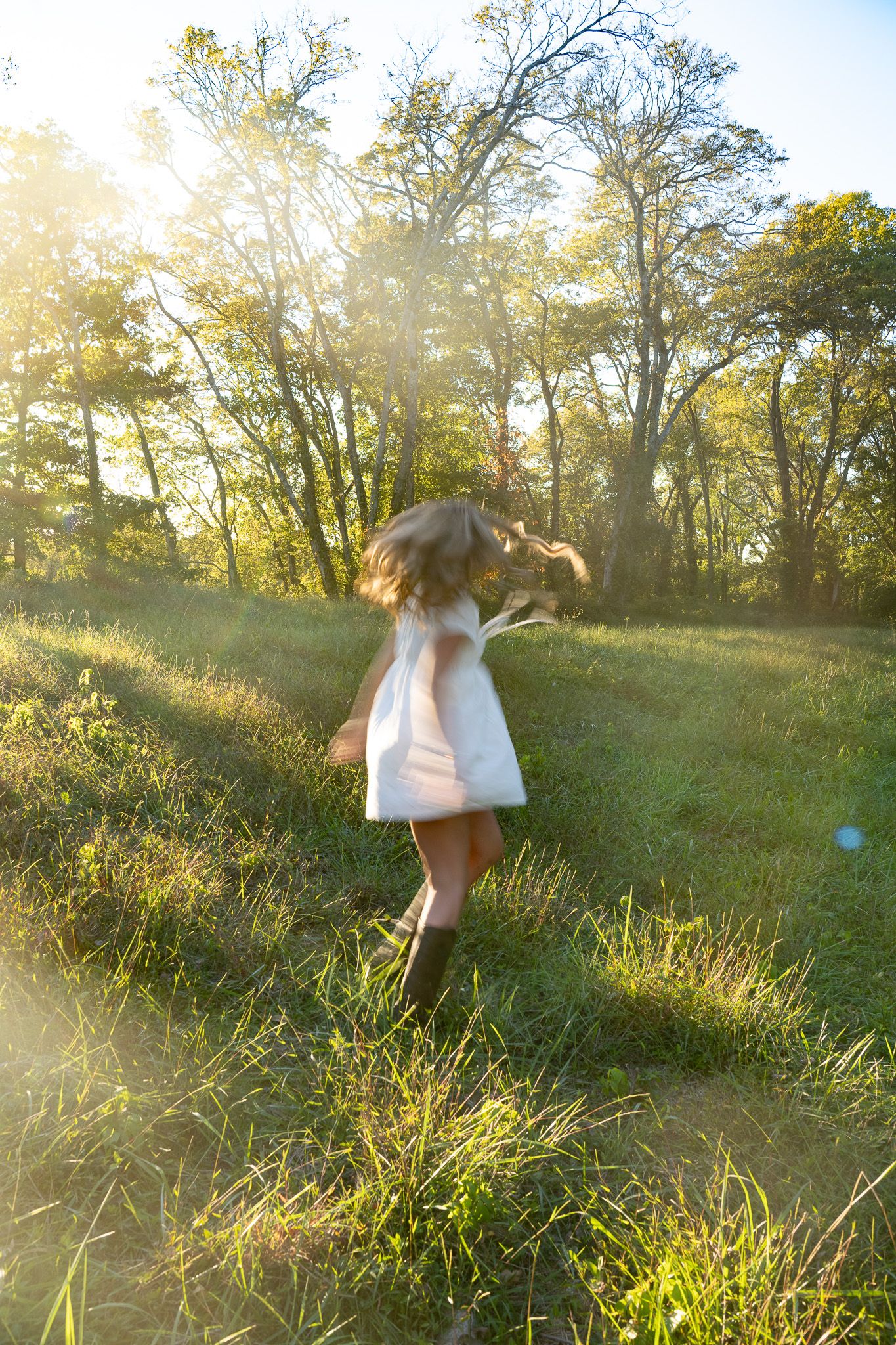 A figure in a flowing white dress twirls through a sunlit meadow at golden hour creating a dreamy ethereal scene.