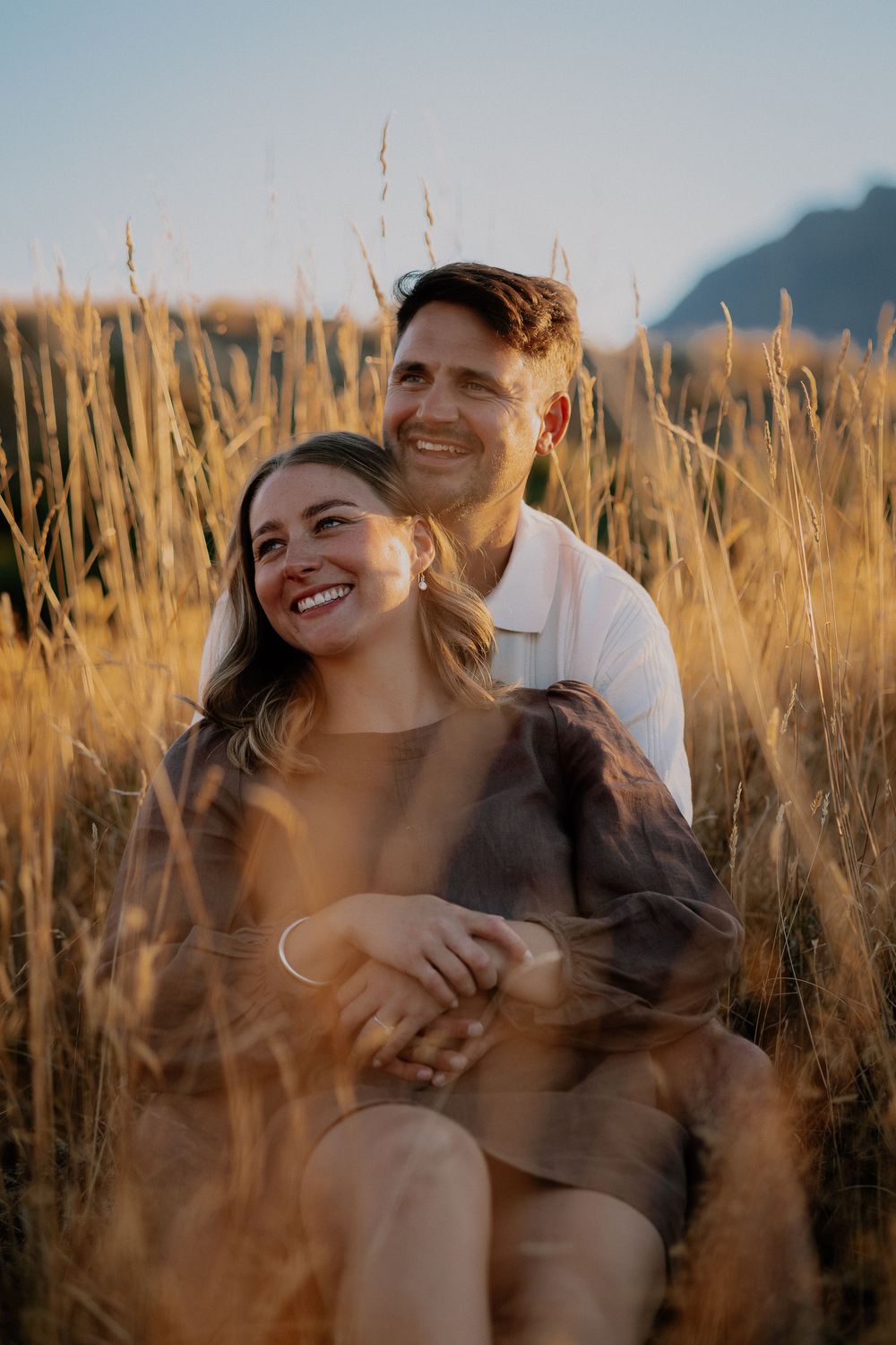 Candid laughter and joy captured between a couple in sun-lit wheat fields at golden hour.
