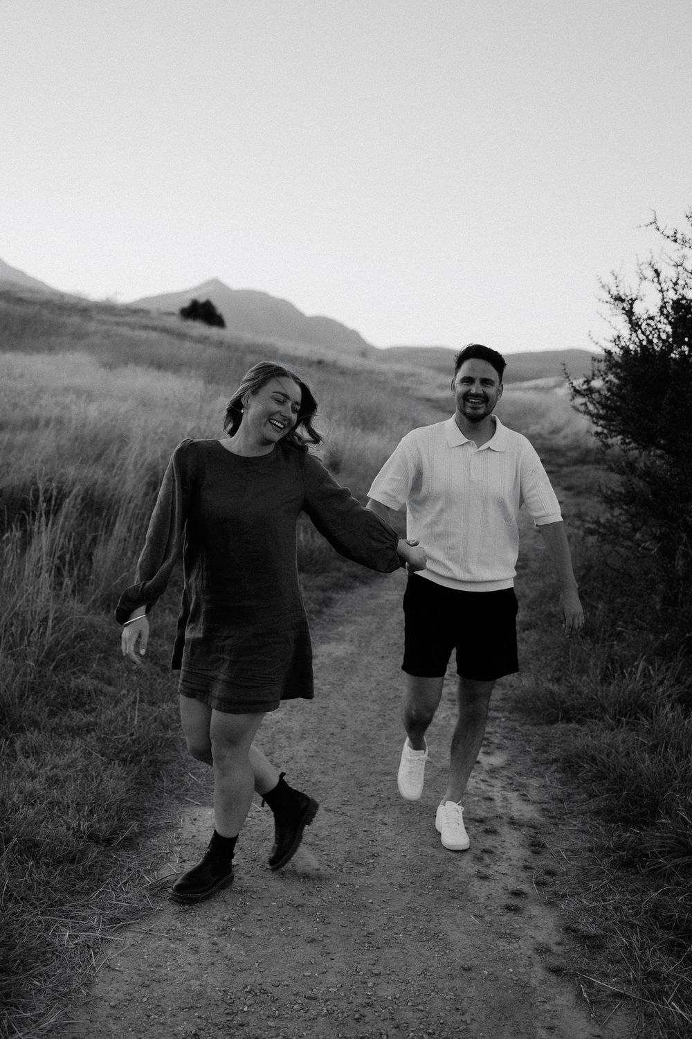 A black and white photo shows two people walking and laughing together on a mountain trail.