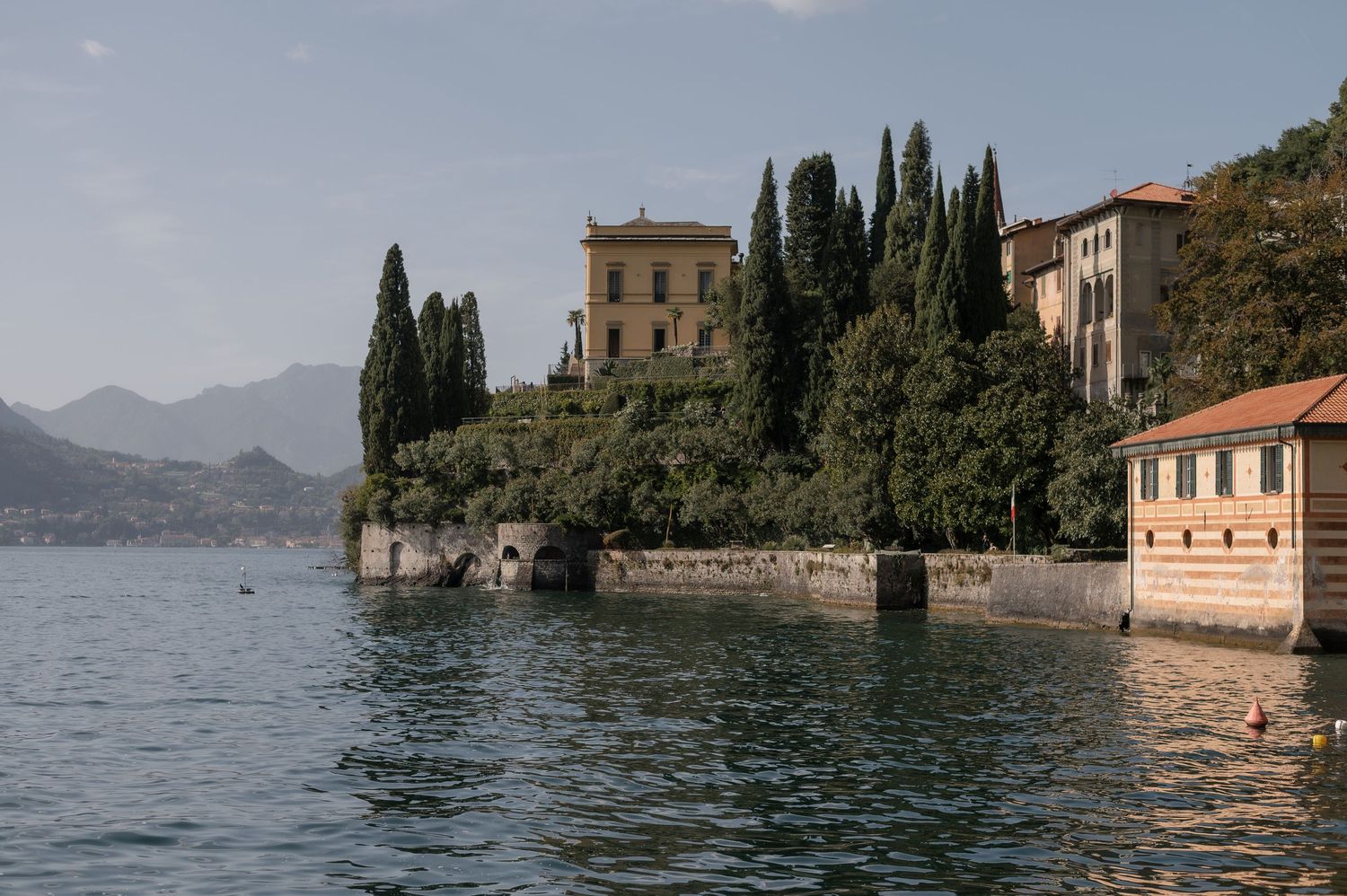 Scenic panoramic view of Lake Como with historic villas and cypress trees along the shoreline in Italy.